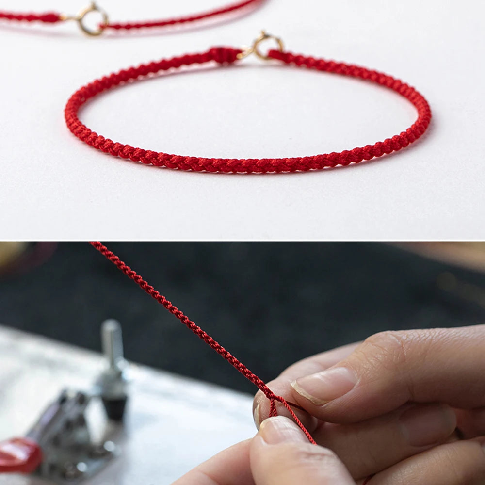 A close-up of a handmade red string bracelet with a gold plated clasp lying on a white surface.