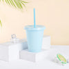 A light blue plastic cold cup with a lid and straw is displayed on a white surface next to ice cubes.