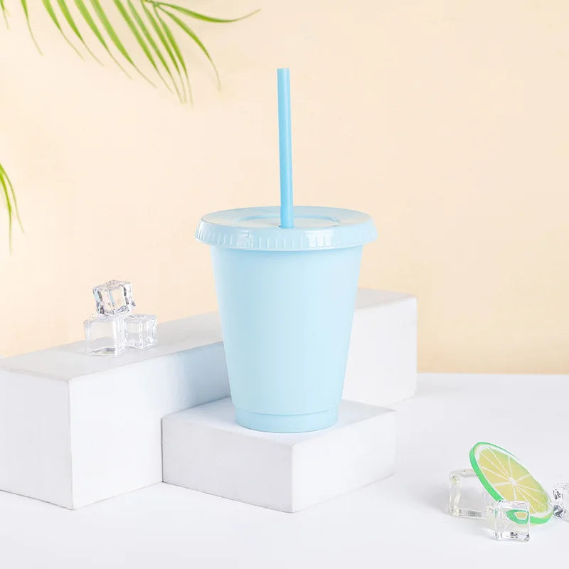 A light blue plastic cold cup with a lid and straw is displayed on a white surface next to ice cubes.