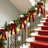 A staircase decorated with evergreen garlands and red velvet bows, accented by gold bells and white snow.