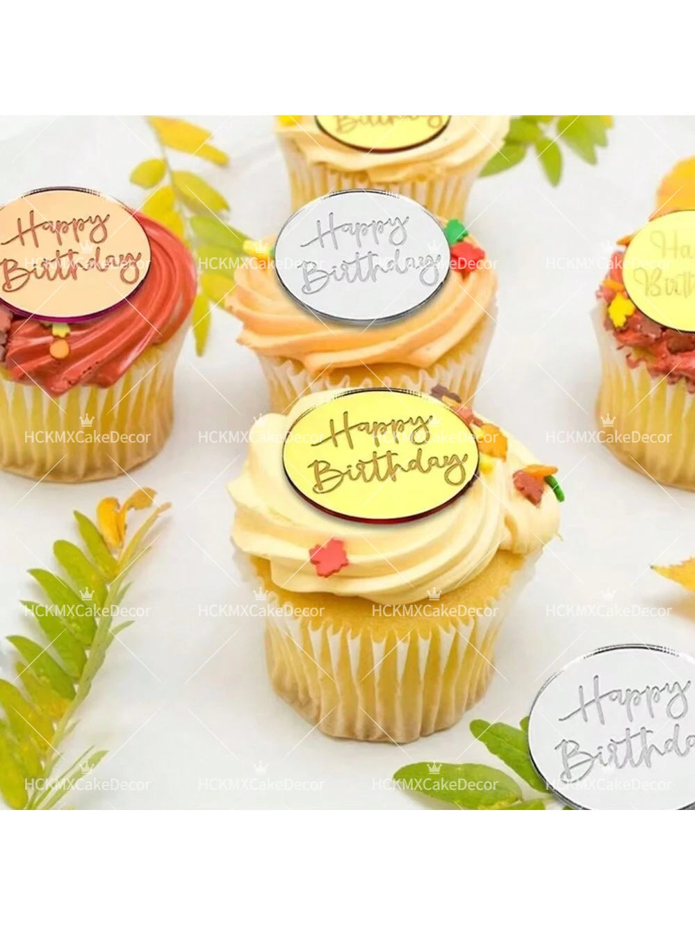 A display of yellow cupcake liners topped with mirror acrylic happy birthday cake toppers and frosting.