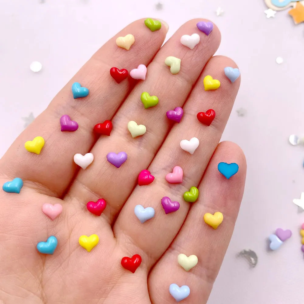 A hand displays a mix of colorful heart-shaped flatback rhinestones for nail art and crafts.