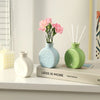 A collection of ceramic mini vases in light blue and green colors with pink flowers on a white shelf.