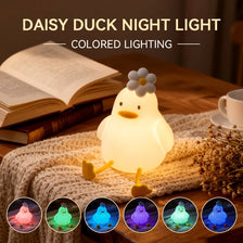 A glowing white duck night light is displayed on a wooden surface next to a book and knitted fabric.