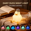 A glowing white duck night light is displayed on a wooden surface next to a book and knitted fabric.