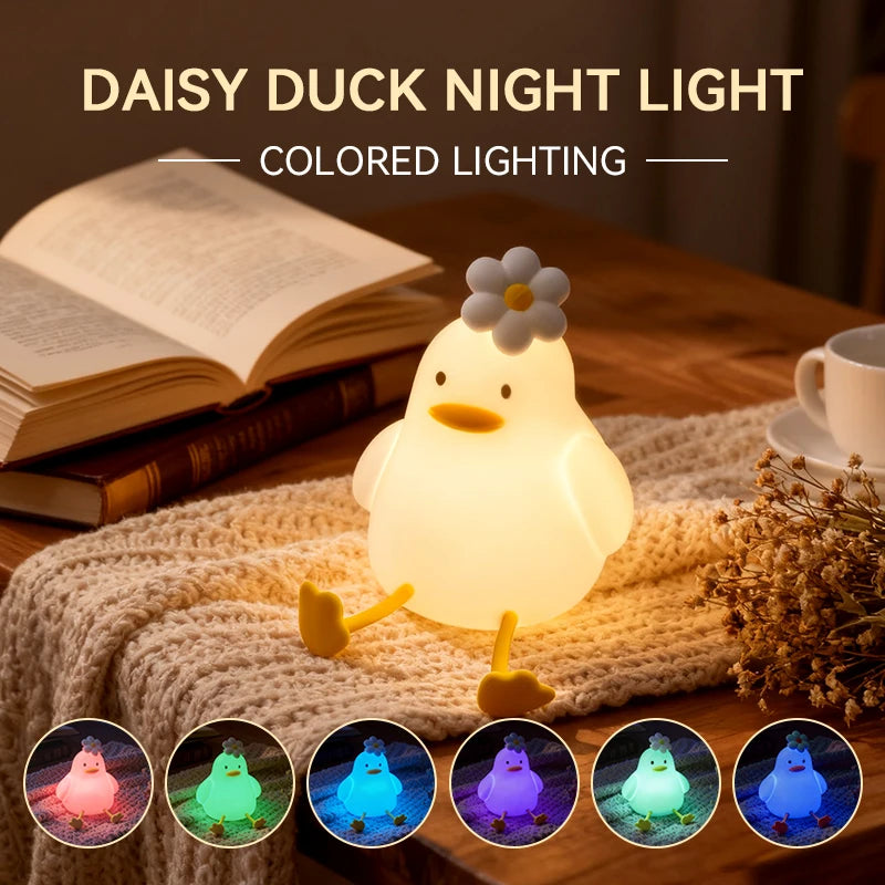 A glowing white duck night light is displayed on a wooden surface next to a book and knitted fabric.