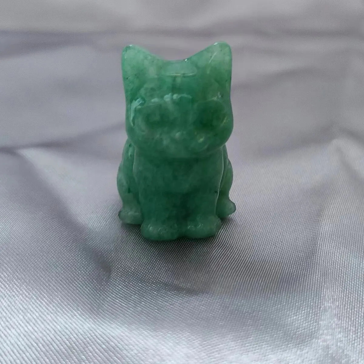 Ornement de chat en cristal vert sculpté à la main sur fond de tissu blanc.
