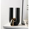 A black and gold U-shaped ceramic tabletop vase displayed on a white shelf.