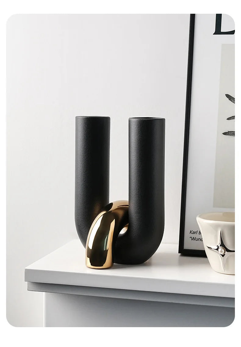 A black and gold U-shaped ceramic tabletop vase displayed on a white shelf.