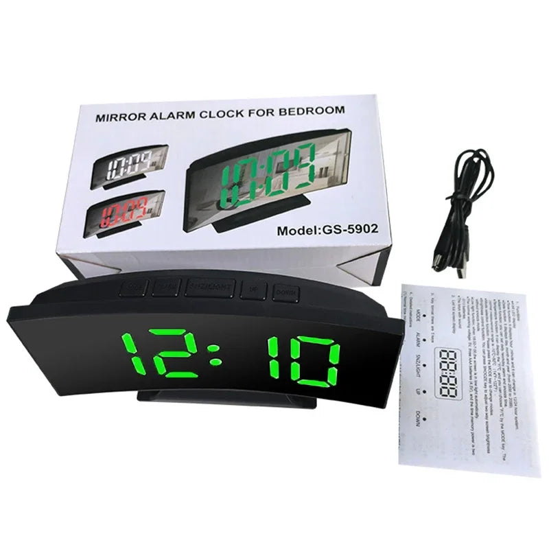 A black LED alarm clock with a digital display showing 12:10 is shown next to its packaging box.