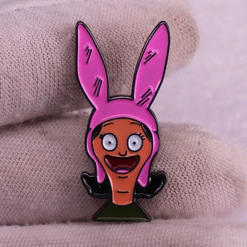 A pink enamel pin badge shaped like a rabbit with a smiling face, held by a hand.