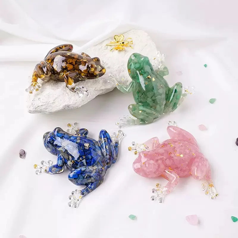 A collection of resin crystal frogs in various colors including amber, green, blue, and pink resting on a white rock.