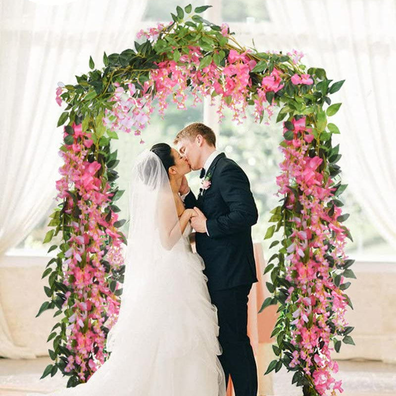 A bride and groom kiss under a floral archway decorated with pink wisteria vines for a wedding ceremony.