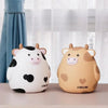A cartoon cow piggy bank coin holder in white and brown colors sitting on a light surface.