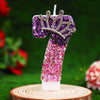 A glitter number 7 birthday candle with a rhinestone crown topper, featuring purple and pink glitter finishes.