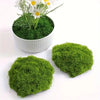 A potted artificial green moss plant with white flowers on a white background.