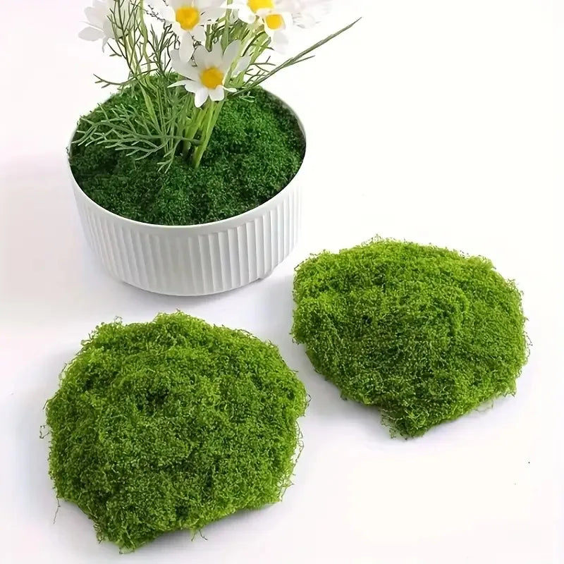 A potted artificial green moss plant with white flowers on a white background.