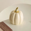 A smooth, cream-colored ceramic pumpkin figurine with a gold stem sits on a white surface.