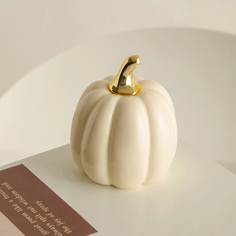 A smooth, cream-colored ceramic pumpkin figurine with a gold stem sits on a white surface.