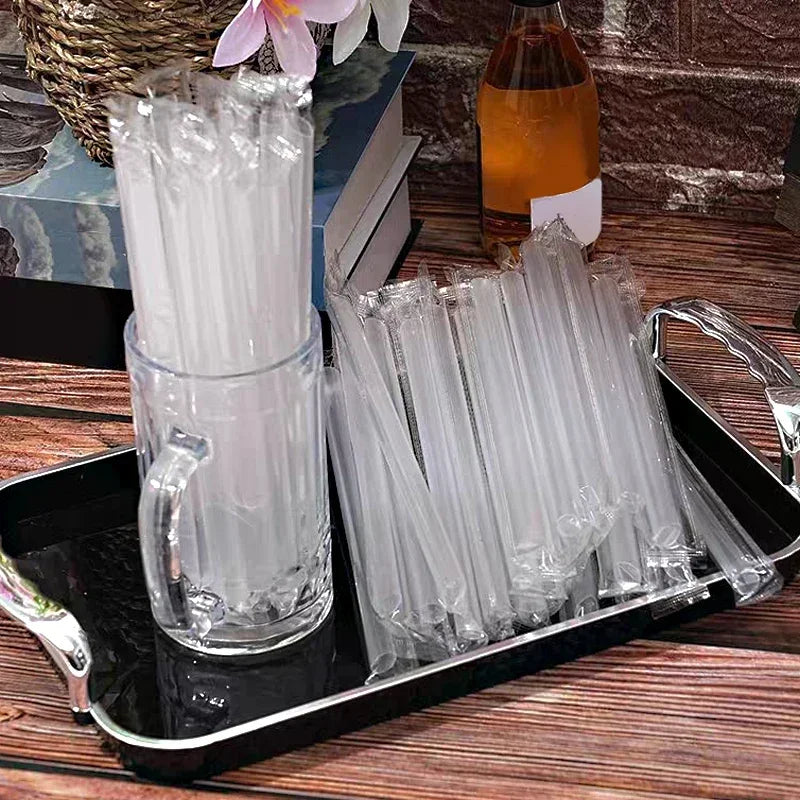 A clear glass jar filled with white disposable plastic straws and a tray of individually wrapped clear plastic straws.