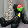 A black figurine of a bear with green skin and pink accents is displayed next to a beige rope decoration.