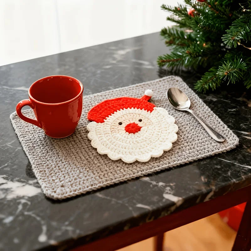 A set of handmade crochet Santa Claus coasters featuring a red and white design placed on a dark marble surface.