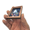 A hand holds a framed picture featuring a white ghost and a black cat among colorful flowers.