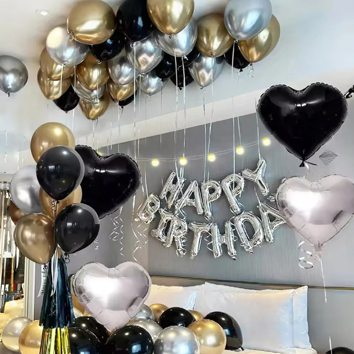 A display of black, gold, and silver balloons with a silver banner shaped like Happy Birthday