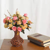 A bouquet of realistic silk rose flowers in shades of pink and cream arranged in a woven vase.