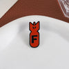 An orange enamel pin shaped like an explosive shark head with the letter F on a white plate.