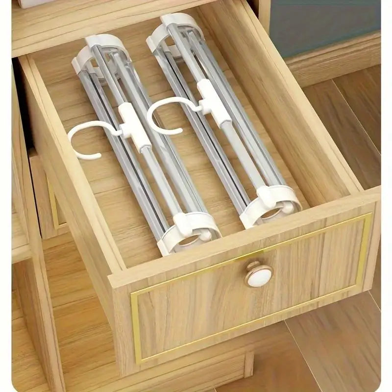 A wooden drawer organizer holding two stainless steel foldable multi-layer pants hangers.