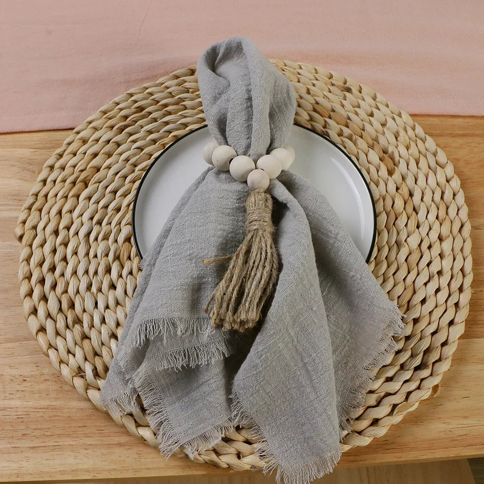 A stack of ten handcrafted fringed cotton napkins in gray are displayed on a round woven mat.