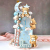 A blue cake decorated with a bear topper, stars, clouds, and cake balls for a baby shower.