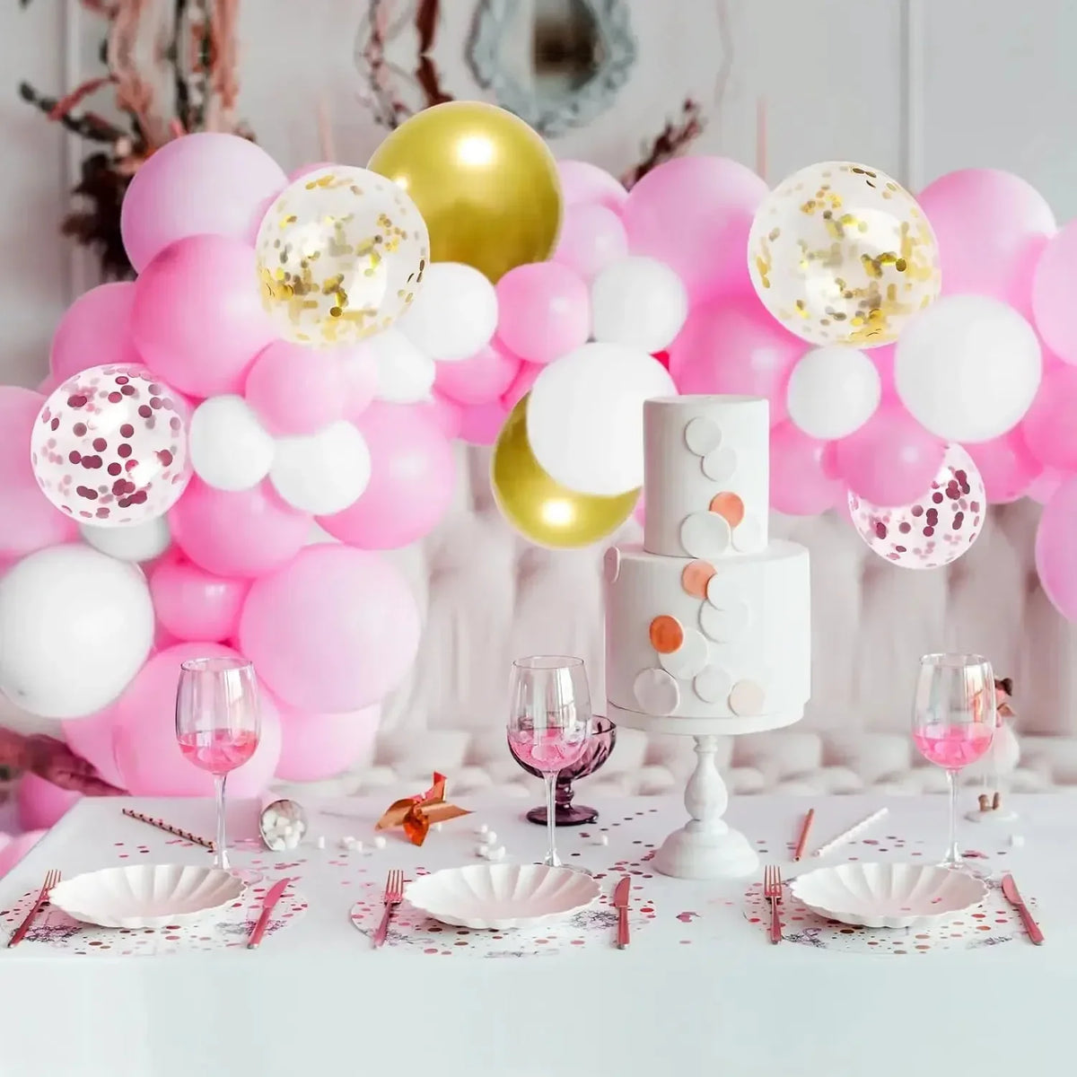 A display of pink and gold confetti latex balloons, including balloons and a tiered cake model.