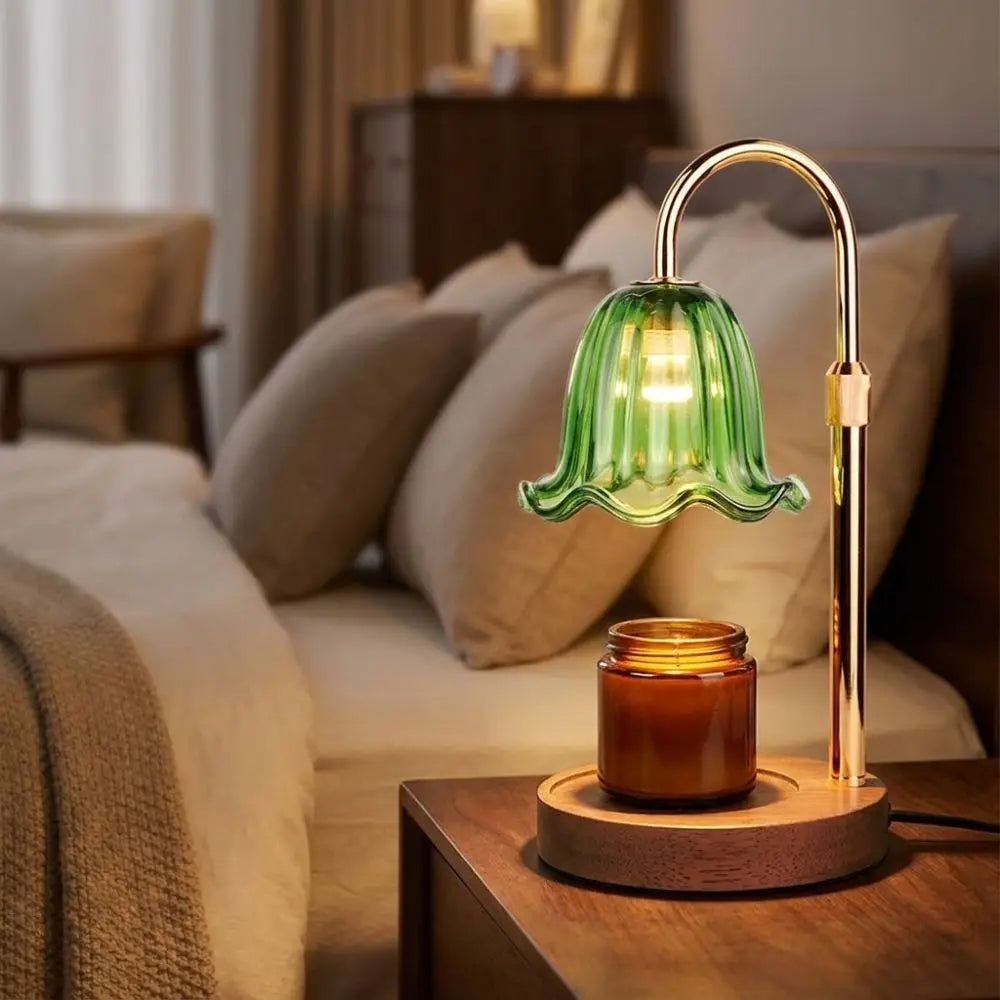 A modern gold-toned adjustable lamp with a green glass diffuser sits on a wooden surface next to a candle jar.
