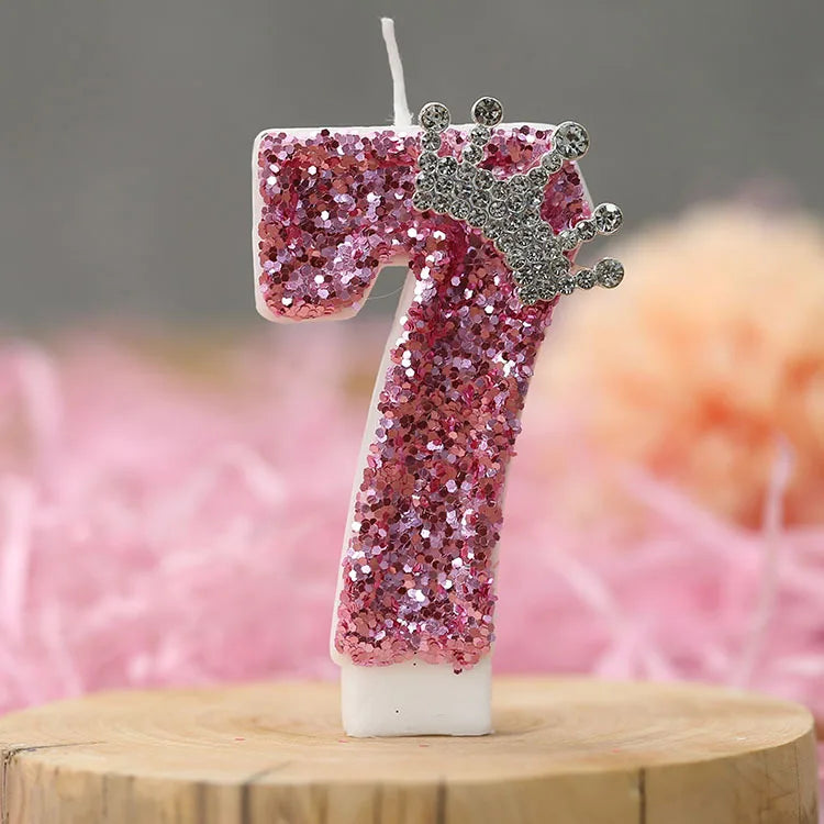 A pink sequin number seven candle with a silver crown topper displayed on a wooden surface.