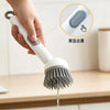 A hand is using an adjustable long-handled liquid washing brush to press and wash food residue from a bowl.