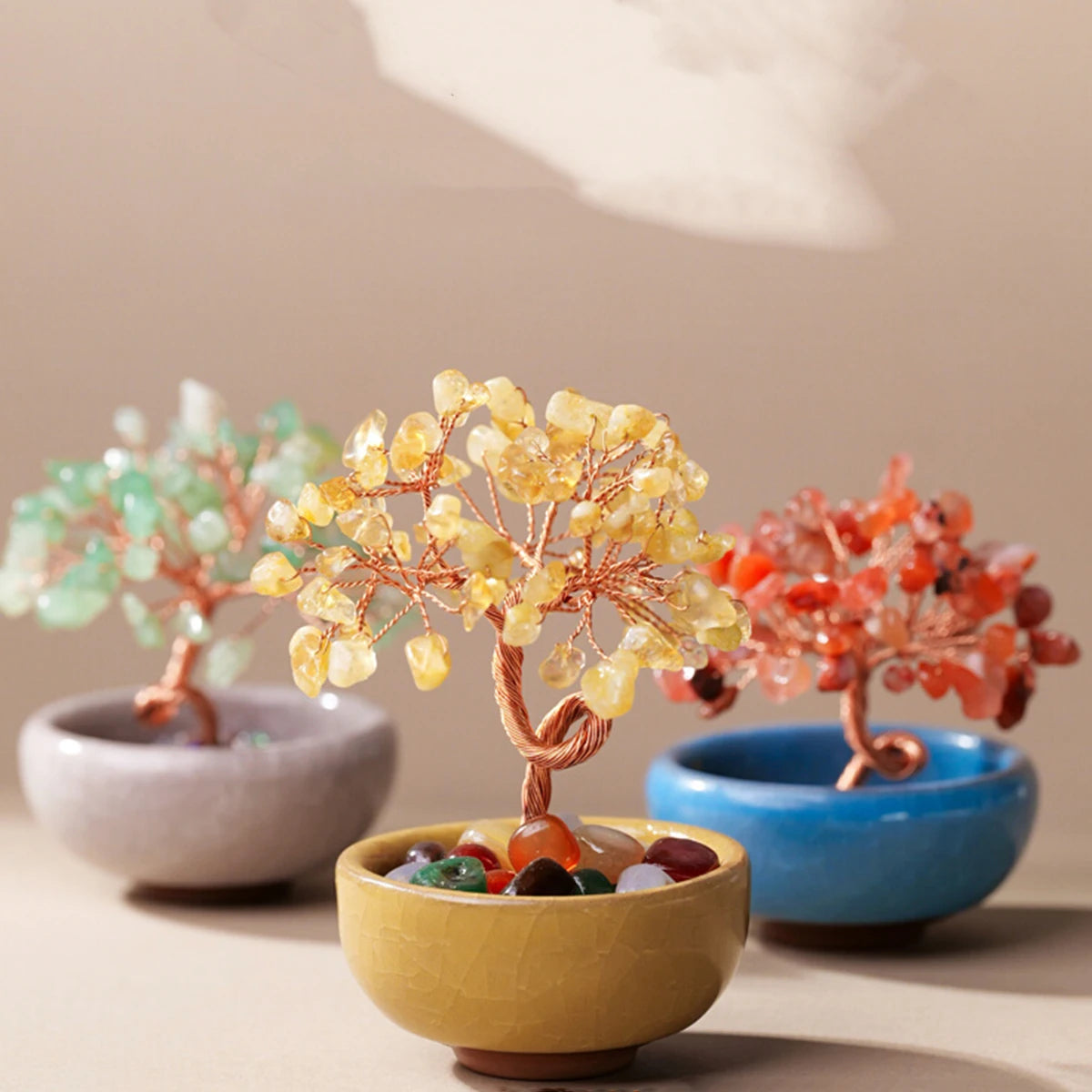 Handcrafted crystal tree with yellow and orange stones on a copper wire base in a light green bowl.