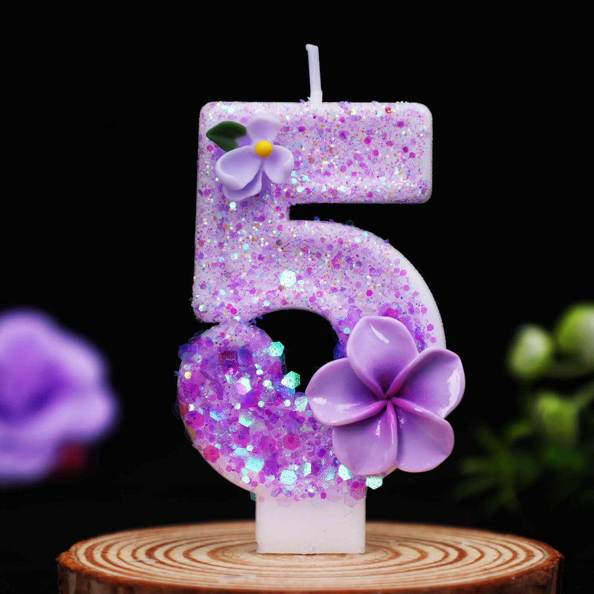 A purple glitter flower number candle shaped like the number 5 on a wooden surface.