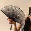 A hand holding an antique style bamboo folding fan with delicate floral patterns against a light background.