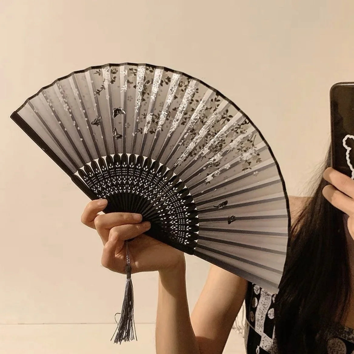 A hand holding an antique style bamboo folding fan with delicate floral patterns against a light background.