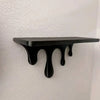 A black drip floating shelf with a unique artistic design mounted on a white wall.
