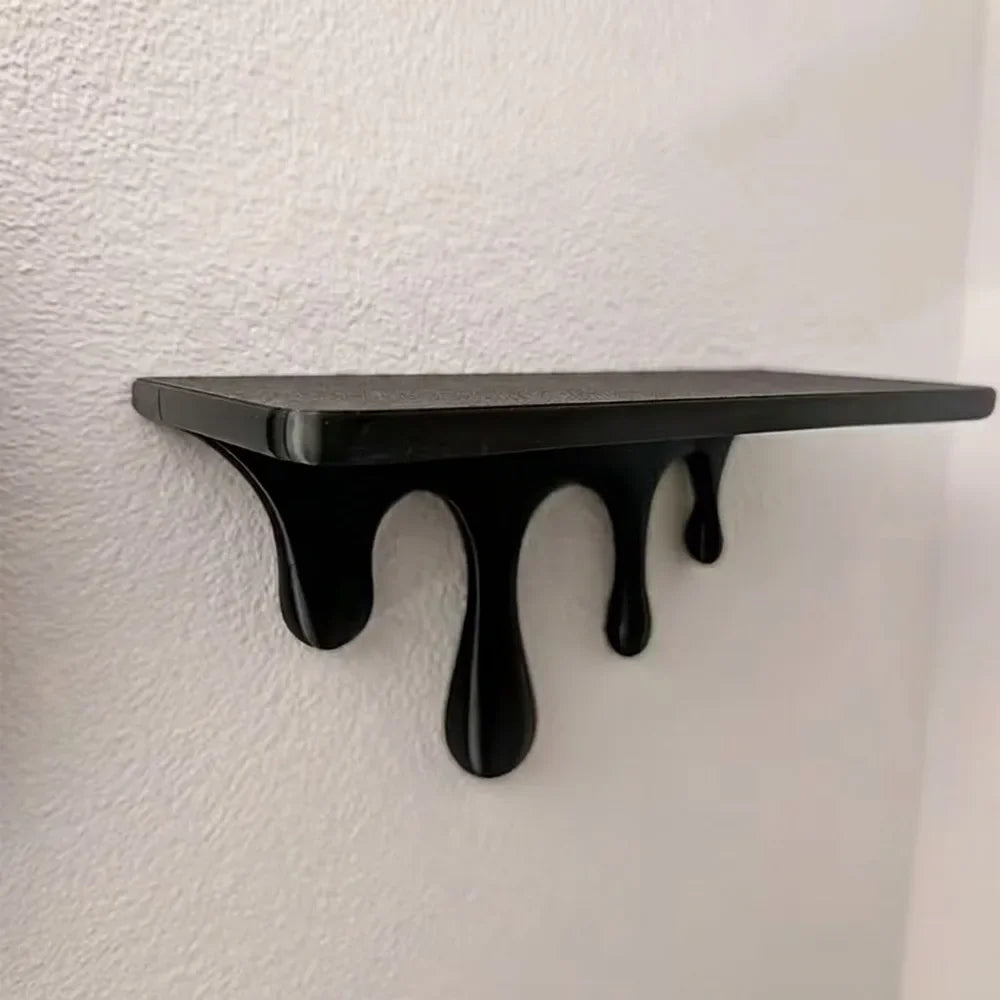 A black drip floating shelf with a unique artistic design mounted on a white wall.