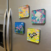 A collection of colorful acrylic fridge magnets featuring floral and whimsical designs.