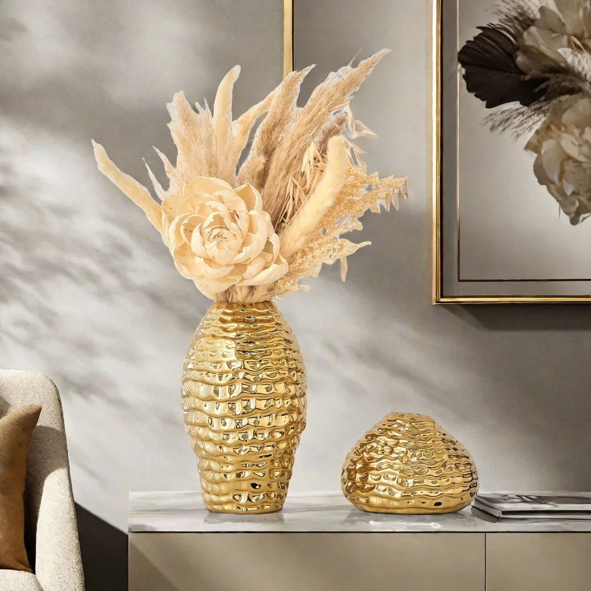 A golden wrinkle ceramic tabletop vase filled with dried floral arrangements sits on a light surface.