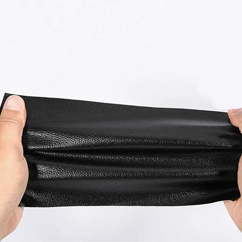 Una mano sostiene un parche de reparación de cuero PU autoadhesivo negro, mostrando su textura y flexibilidad.