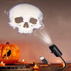An orange pumpkin and a white skull are illuminated by a projector light in a dark setting.