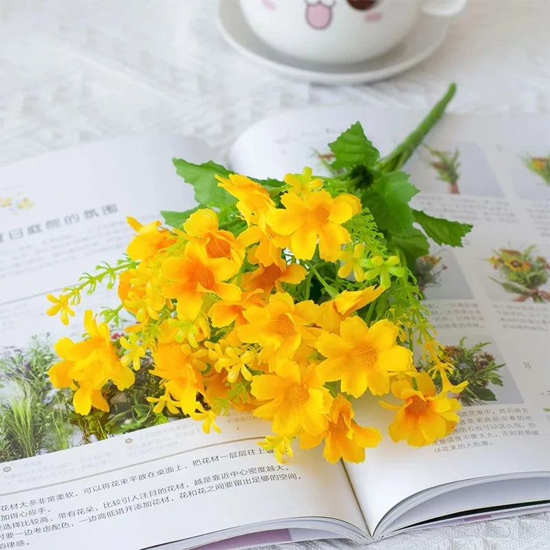 A bouquet of bright yellow artificial daisy flowers with green leaves displayed on an open book.