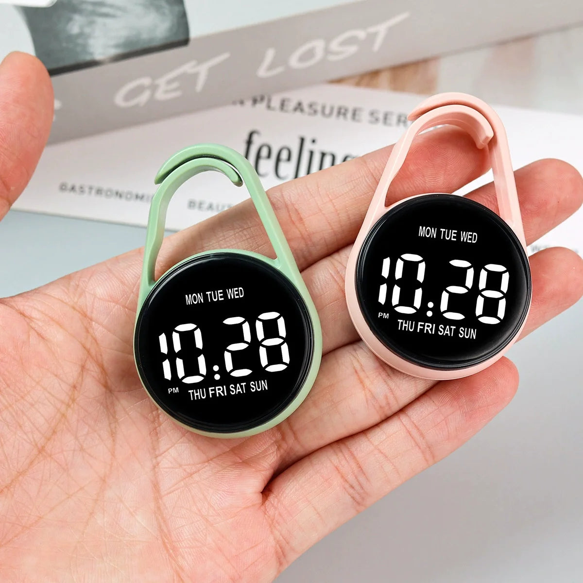 A hand holds a pink LED pocket watch with a black face displaying 10:28 and a green-colored watch case.