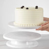 A white layer cake with dark berries on top displayed on a white cake board.